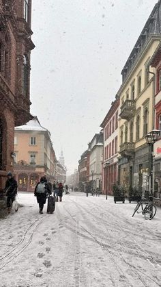 people walking down a snowy street with buildings in the background