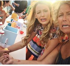 two women sitting at a table with food and drinks in front of them, making funny faces