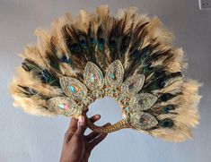 a person holding a peacock feather fan in front of a white wall with blue, green and gold feathers