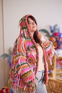 a woman wearing a crocheted jacket and holding a cup in her hand while standing next to a wicker chair