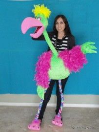 a woman standing in front of a blue wall holding a pink and green stuffed animal