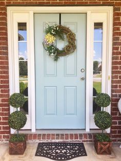 a blue front door with two potted plants and a wreath