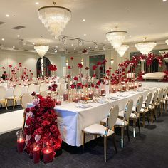 a banquet hall with tables and chairs covered in red flowers, candles and centerpieces