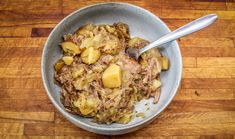 a bowl filled with meat and potatoes on top of a wooden table next to a spoon