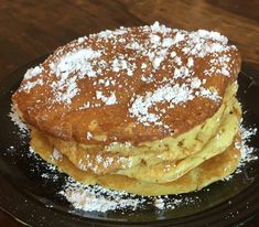 a stack of pancakes covered in powdered sugar on top of a black platter