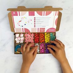 a child's hands are playing with colorful beads in an open box on a marble surface