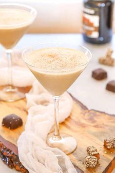 two glasses filled with liquid sitting on top of a wooden table next to chocolate candies