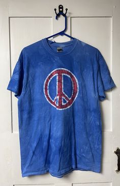 The peace sign is back, and it's everywhere! On this patriotic peace sign shirt, I drew a big, funky peace sign and painted it red before dyeing the shirt bright blue. This shirt was made using a size large Gildan brand adult T-shirt. It's a patriotic color combination! 100 percent cotton, short sleeves. Ready to ship! Peace, Baby! Batiks are one-of-a-kind, hand-dyed garments for kids and kids at heart. I design for fun, so I look for cute graphics and bold colors. Each shirt I create is unique - the dye never takes the same way twice, and the cracks in each design are always different. All of my garments are 100 percent cotton and prewashed in an additive-free detergent, so they're preshrunk by the time they get to you. Care: Wash in cold with like colors. Blue Cotton T-shirt For Festivals, Blue Cotton Hippie T-shirt, Blue Hippie Cotton T-shirt, Cotton Peace Sign Short Sleeve T-shirt, Cotton Short Sleeve T-shirt With Peace Sign, Casual Cotton T-shirt With Peace Sign, Casual Short Sleeve Tops With Peace Sign, Peace Sign Shirt, Peace Sign Shirts