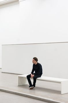 a man is sitting on a bench in an empty room with no one around him