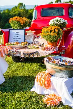 an old red truck parked next to a table filled with food and flowers on the grass