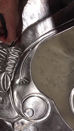 a person is using scissors to cut into a metal plate with decorative designs on it