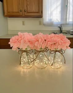 three mason jars filled with pink flowers sitting on top of a counter