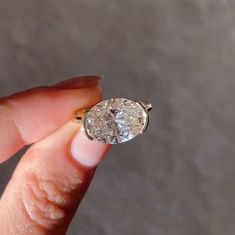 a woman's hand holding a ring with a large diamond on the middle of it