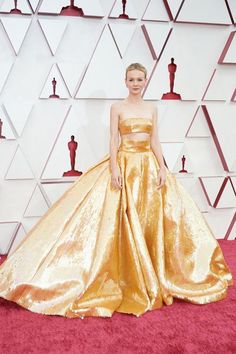 a woman in an orange and gold gown standing on a pink carpet at the oscars