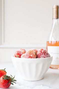 a white bowl filled with powdered sugar covered strawberries next to a bottle of wine