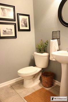 a white toilet sitting next to a sink in a bathroom under a mirror and pictures on the wall