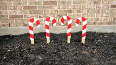 three red and white candy canes sitting in front of a brick wall on top of mulch