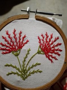 a person holding up a small embroidery hoop with red flowers on it and green stems