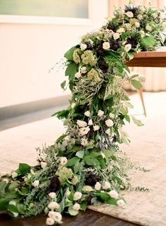 an arrangement of flowers and greenery is arranged on the floor in front of a table