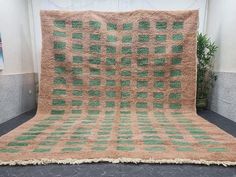 a green and beige blanket sitting on top of a black floor next to a potted plant