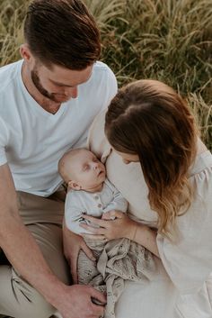 a man and woman are holding a baby in their lap while sitting on the ground