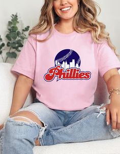 a woman sitting on top of a white couch wearing a pink shirt with the word phillies