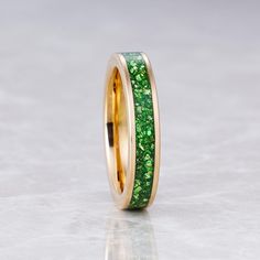 a gold ring with green glitter inlays on the outside and inside, sitting on a white surface