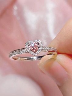 a close up of a person's hand holding a ring with a pink diamond