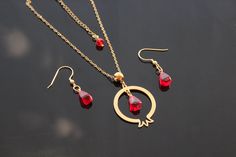 This stunning pomegranate-inspired jewelry set features 14K gold-plated stainless steel parts, including a polished circular pomegranate-shaped pendant and delicate matching earrings. Each piece is adorned with vibrant glass beads that resemble pomegranate seeds, adding a rich pop of red color. The necklace's pendant hangs from a sleek gold-plated chain, giving it a minimalist yet elegant look. The earrings follow the same design motif, with teardrop-shaped glass seed beads that catch the light beautifully. This set reflects a perfect balance of timeless elegance and cultural symbolism, making it ideal for special occasions or as a meaningful gift. 14K gold-plated stainless steel components for durability and a luxurious finish. Circular pomegranate-shaped pendant with smooth edges. Vibran Pomegranate Gold Jewelry, Pomegranate Pendant, Pomegranate Earrings, Pomegranate Jewelry, Pomegranate Seeds, Inspired Jewelry, Red Glass, Matching Earrings, Meaningful Gifts