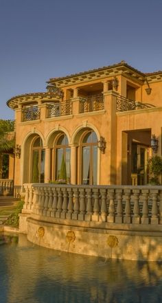 a large house sitting next to a body of water with a fountain in front of it