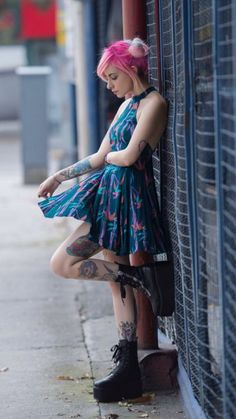 a woman with pink hair and tattoos leaning against a wall on the side of a street