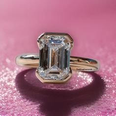 an emerald - cut diamond ring sits on a pink background