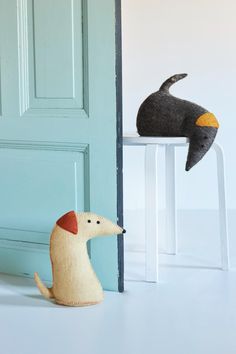 two stuffed animals sitting on stools in front of a blue door with a cat and bird