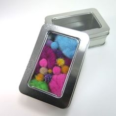 a tin with some colorful pom - poms in it next to a metal container