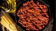 a skillet filled with spaghetti and sauce on top of a wooden table next to a bottle