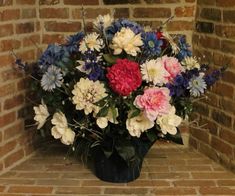 a vase filled with lots of colorful flowers on top of a brick floor next to a wall