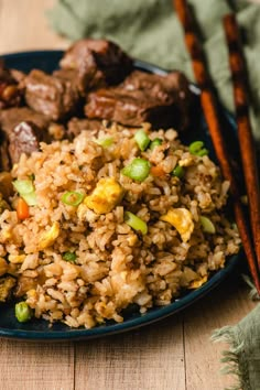 a plate filled with rice and meat on top of a wooden table next to chopsticks