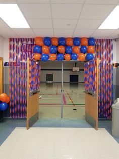 an indoor basketball court with orange and blue balloons on the wall, as well as two sets of doors