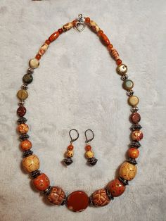 This necklace centers around a banded orange agate bead and features painted wood beads, round orange quartzite beads, picasso jasper coin beads, and silver plated lantern beads. Adjustable Orange Czech Glass Necklace, Artisan Orange Jewelry With Wooden Beads, Orange Jewelry With Round Wooden Beads, Unique Orange Jewelry With Wooden Beads, Orange Jewelry With Wooden Beads For Gifts, Artisan Orange Round Bead Jewelry, Orange Jewelry With Wooden Beads As A Gift, Orange Wooden Beaded Jewelry, Artisan Orange Jewelry With Round Beads