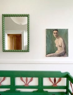 a green bench sitting in front of a painting on the wall next to a mirror