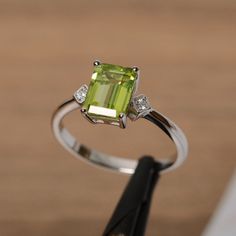 It is a natural peridot ring. The main stone is 6 mm*8mm emerald cut peridot, weight about 1.68 carats. The basic metal is sterling silver and plated with rhodium. To change the metal to a solid gold (white/rose) or platinum is also available, please ask for a quotation if you want. You can also go to my shop Home for more elegant rings: https://www.etsy.com/shop/godjewelry?ref=hdr_shop_menu Ruby is the birthstone of August, it will be a great gift for your lover! More peridot rings: https://www August Birthstone Ring, Promise Ring For Her, Quince Ideas, August Birthstone, Promise Rings For Her, Sterling Silver Engagement Rings, Peridot Ring, July Birthstone, August Birth Stone