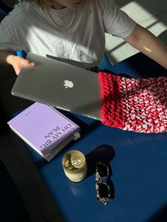 a woman sitting at a table with an apple laptop and other items on her lap