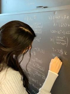 a woman writing on a blackboard with lots of calculations written all over the board