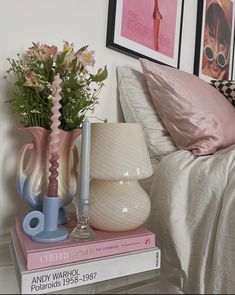 two vases with flowers are on top of books in front of a lamp and pictures