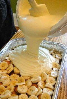 a pan filled with bananas and cream being drizzled on top of it