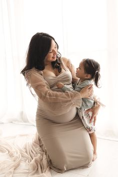 a woman holding a baby in her arms and sitting on the floor next to a window