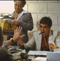 three men sitting at a table with papers and money in front of them, one man is holding his hand out to the other