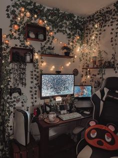 a computer desk topped with a monitor and a keyboard next to a plant covered wall