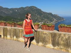 a woman in a colorful dress is standing on a balcony overlooking the ocean and mountains