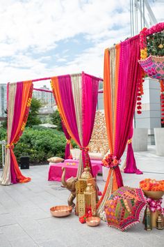 an outdoor wedding setup with pink and orange draping, gold decorations and candles